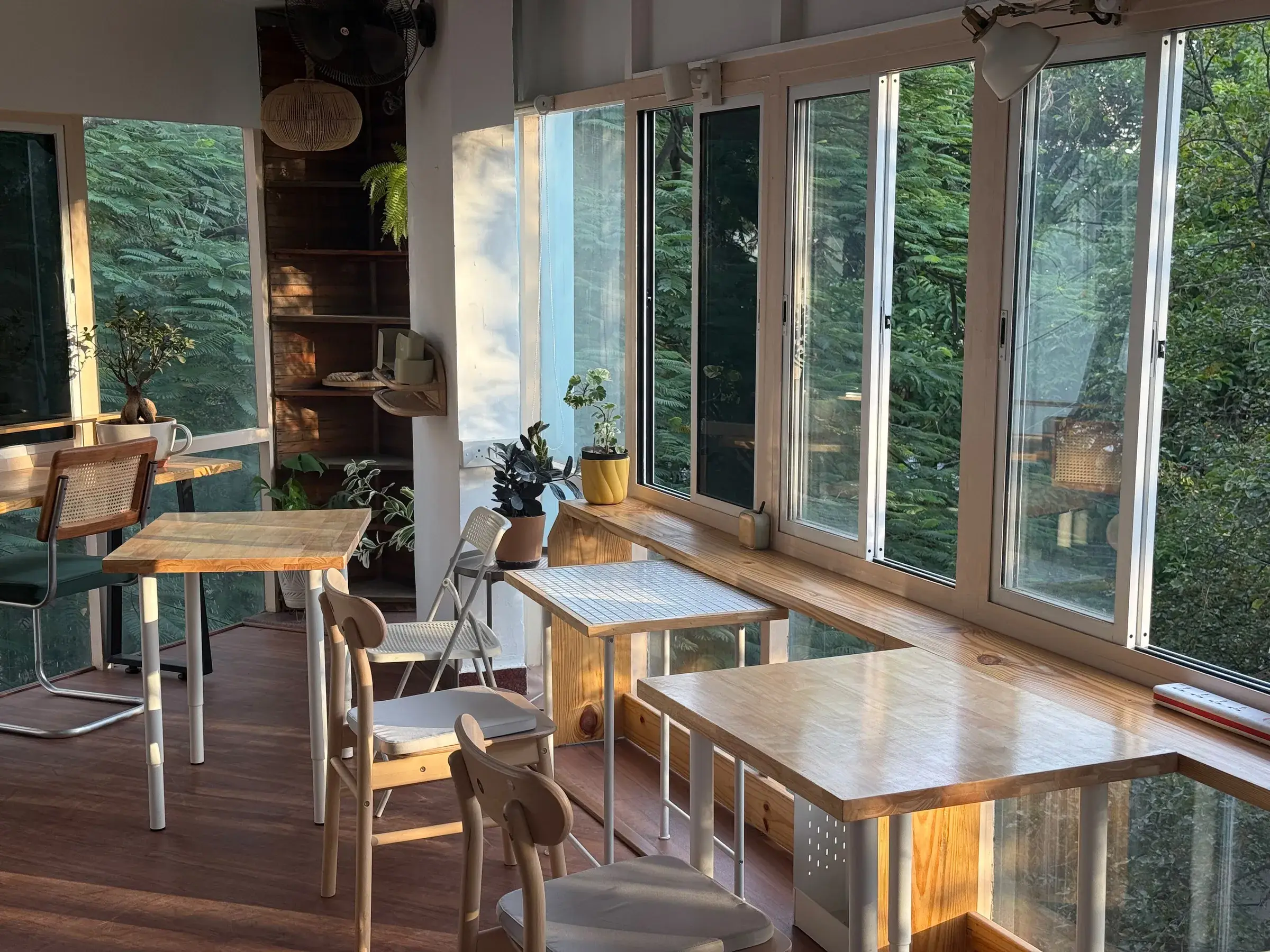Bright corner of the room with wooden tables, white chairs and tall windows onto the trees