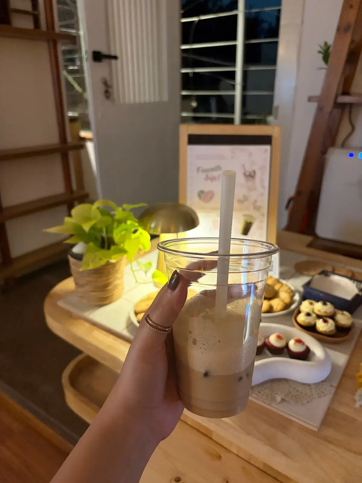 An iced coffee held over the pop-up table, the lamp and poster softly blurred behind